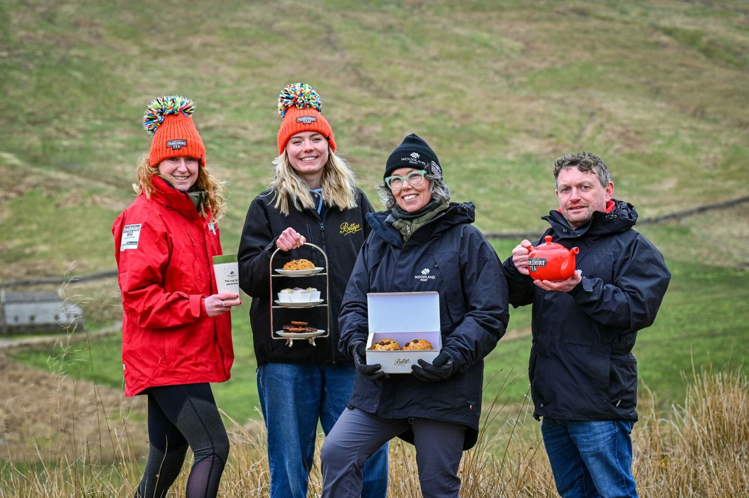 A group of people smiling to the camera holding various cakes and drinks in the Yorkshire Dales