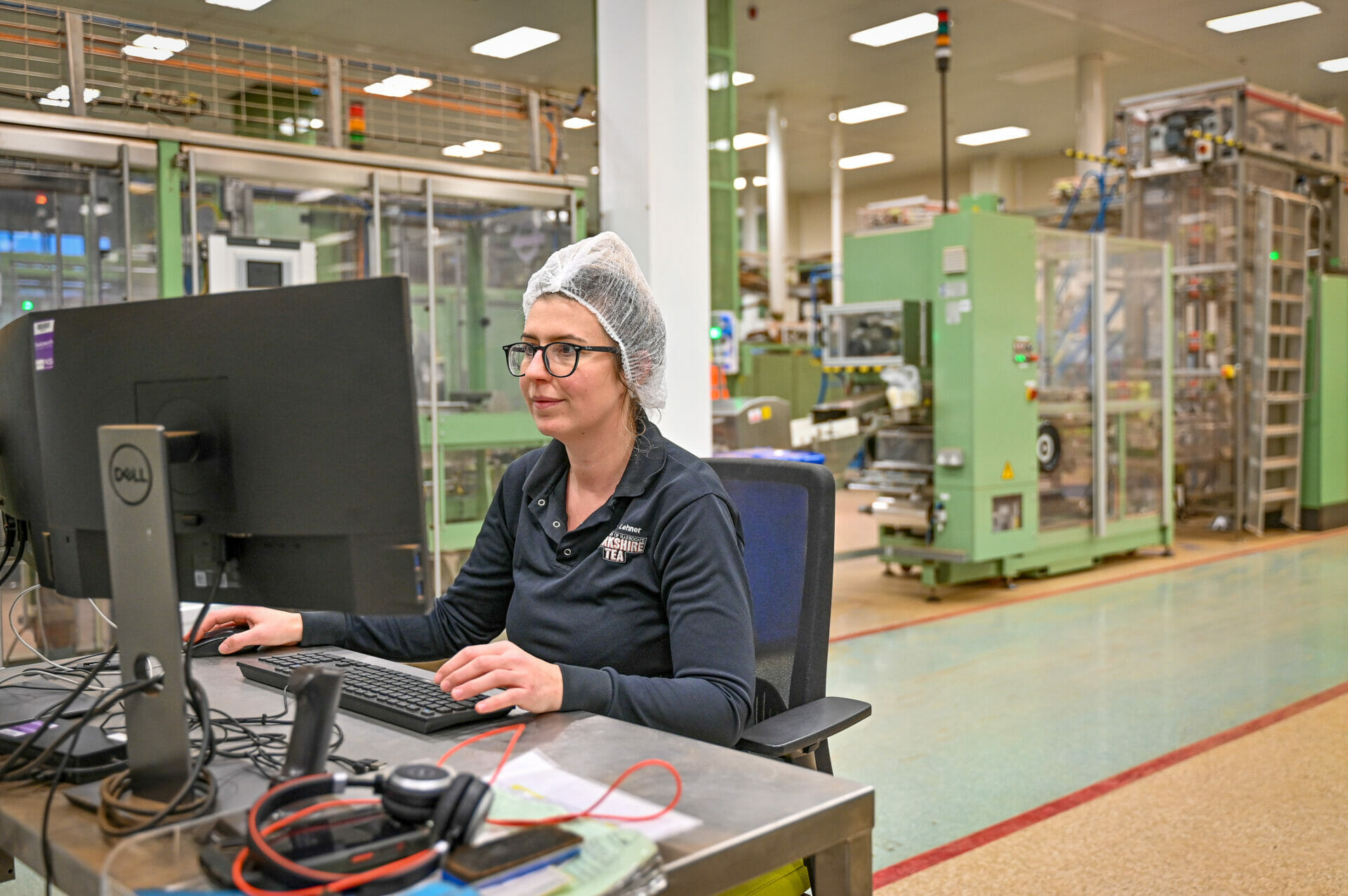 A female duty manager working at a computer with some machinery in the background.