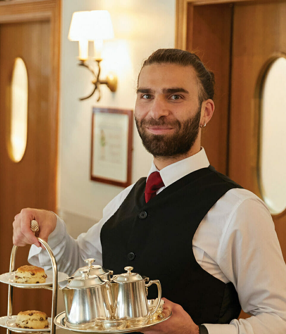 a male waitor holding a portion of afternoon tea