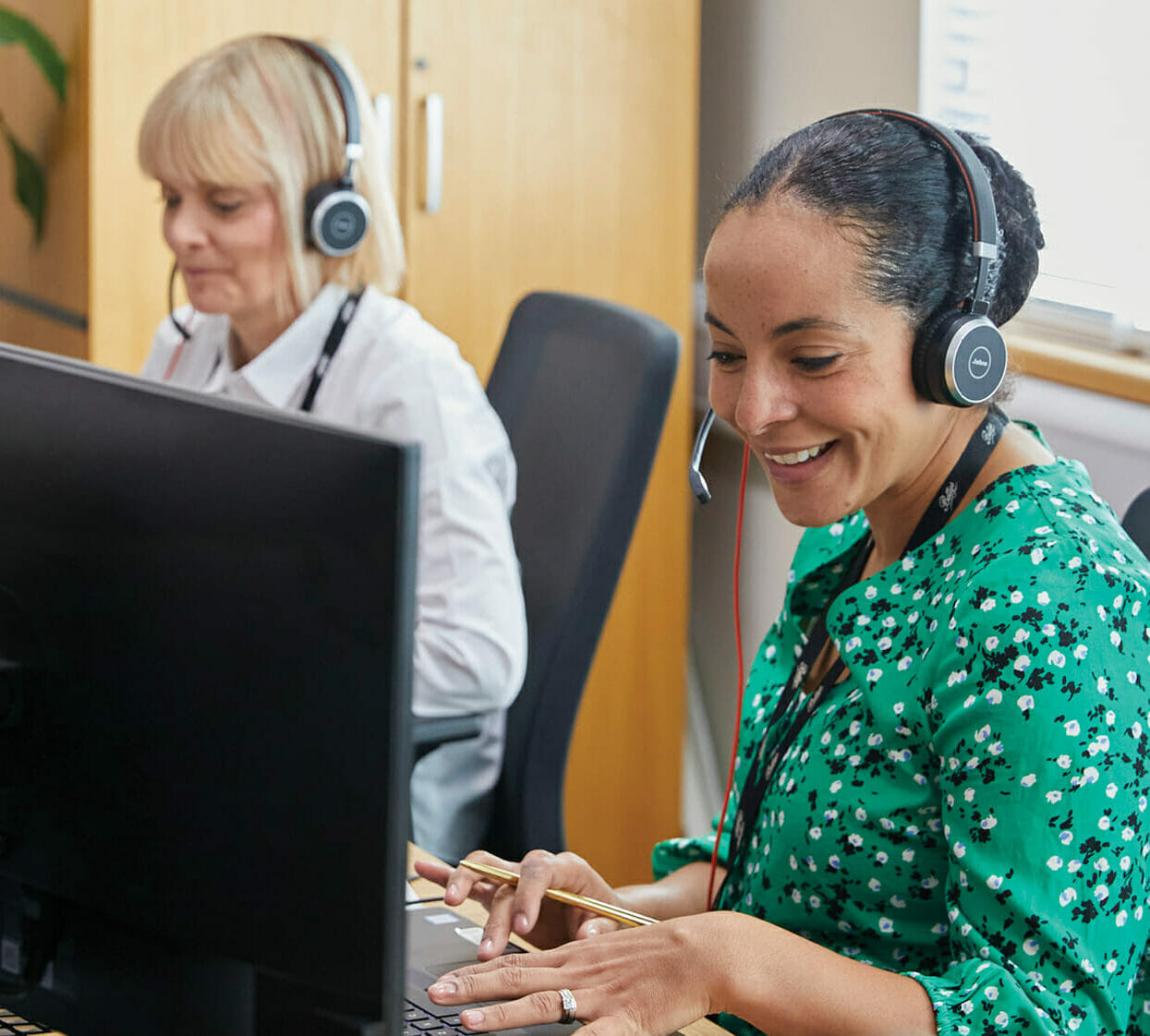 two women in an office settings wearing headsets talking to customers