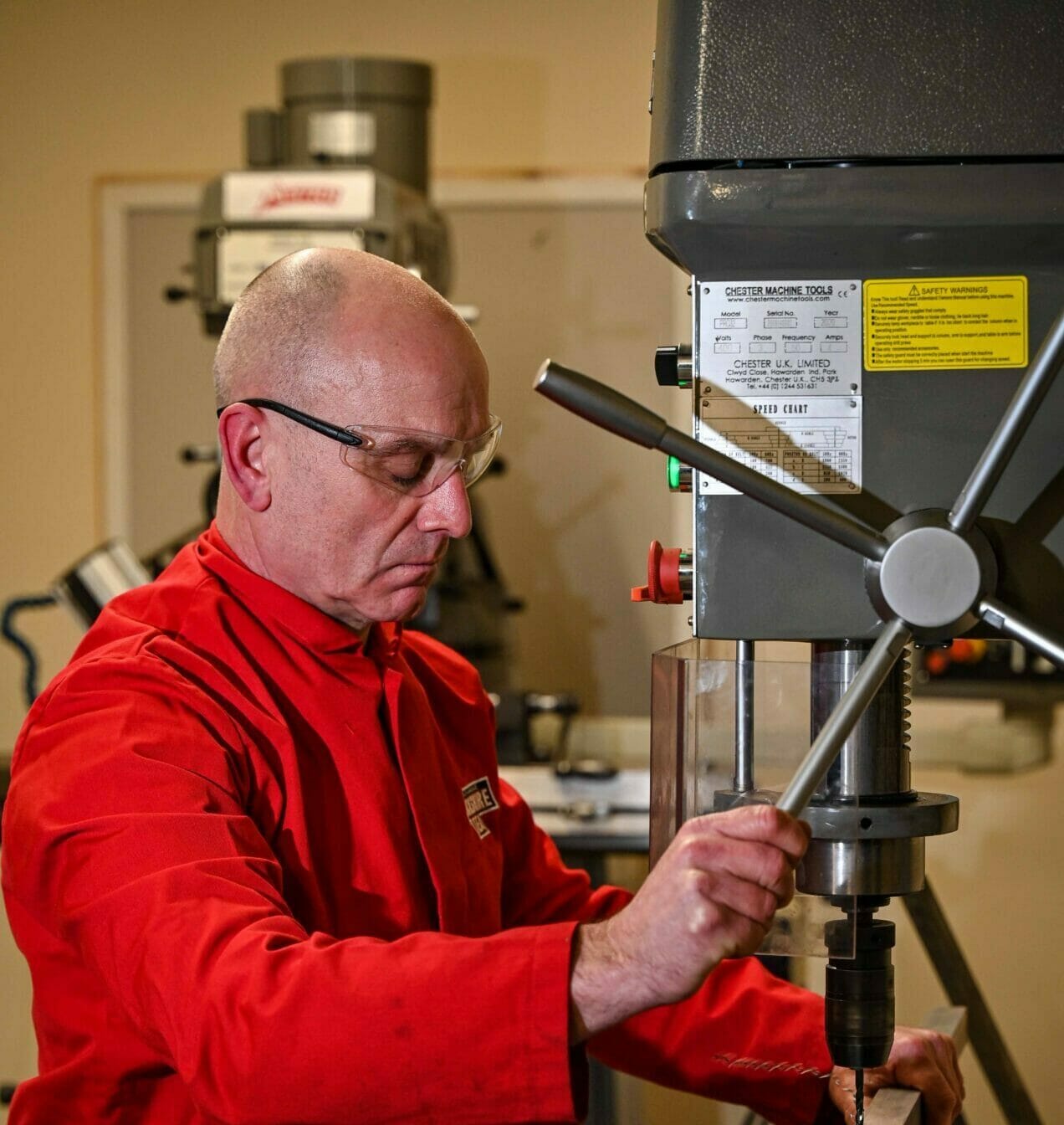 A man wearing safety goggles operating equipment in an engineering workshop.