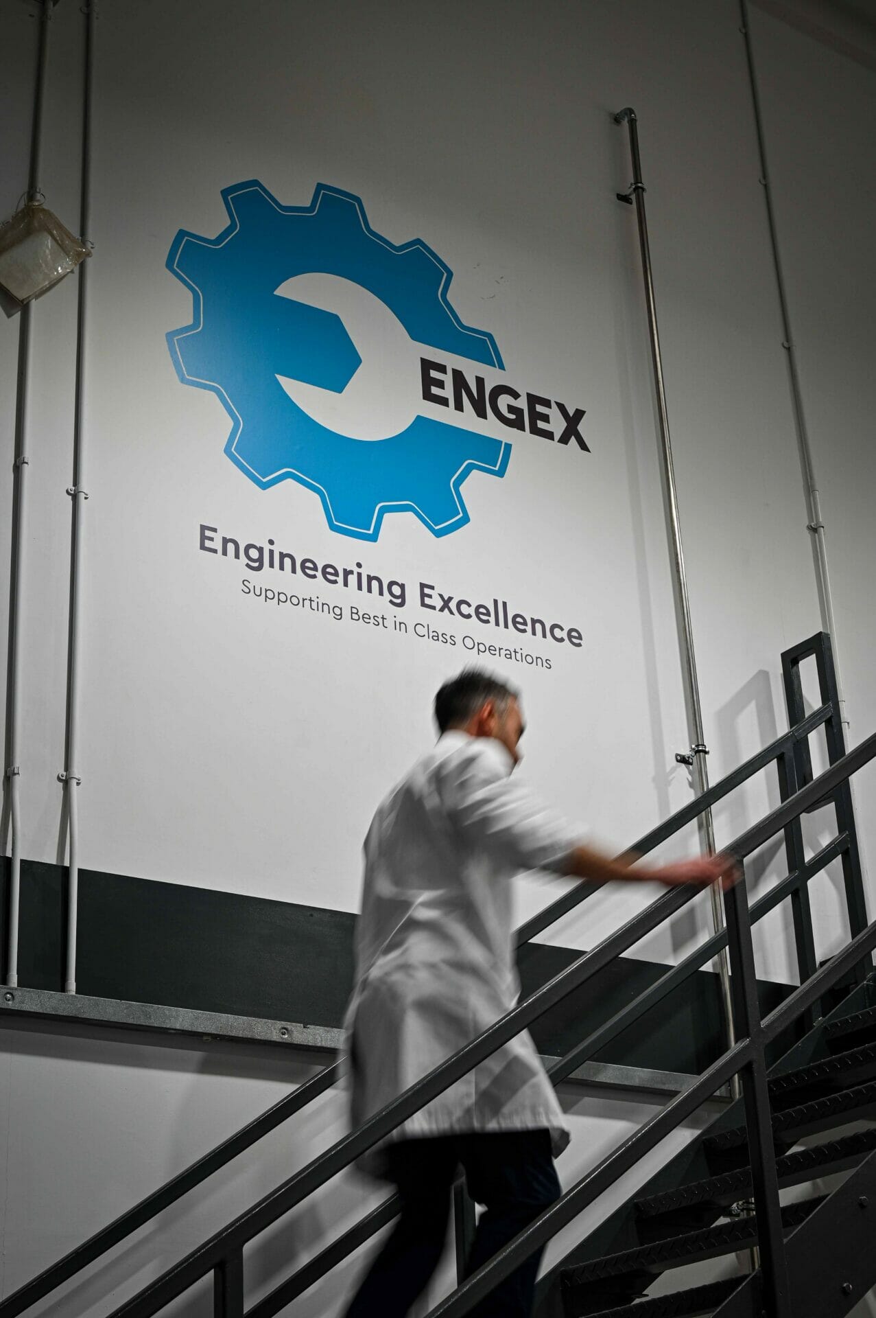 A man wearing a lab coat walking upstairs past a sign that says 'Engineering Excellence'