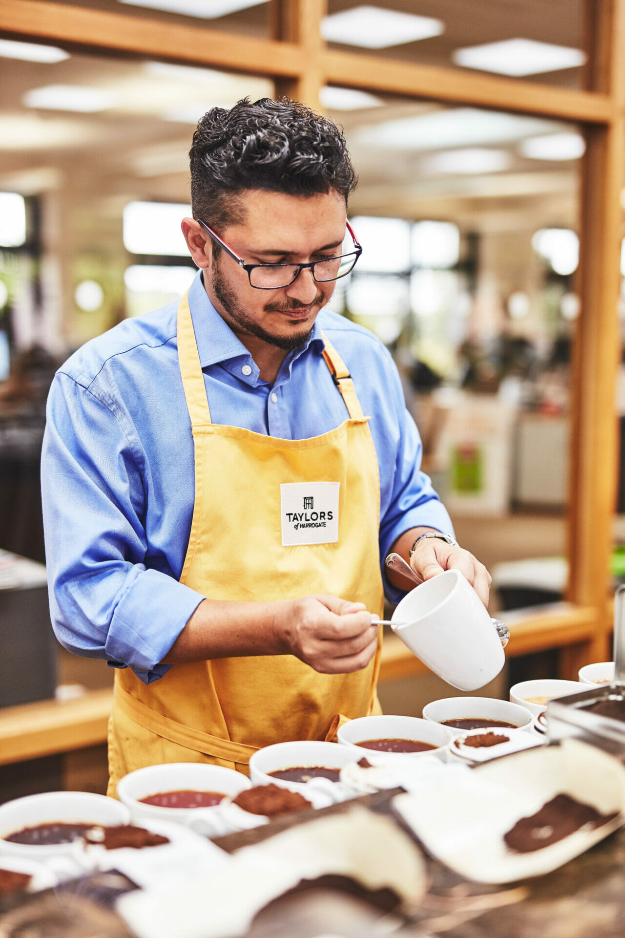 A man wearing an apron tasting tea with a spoon.