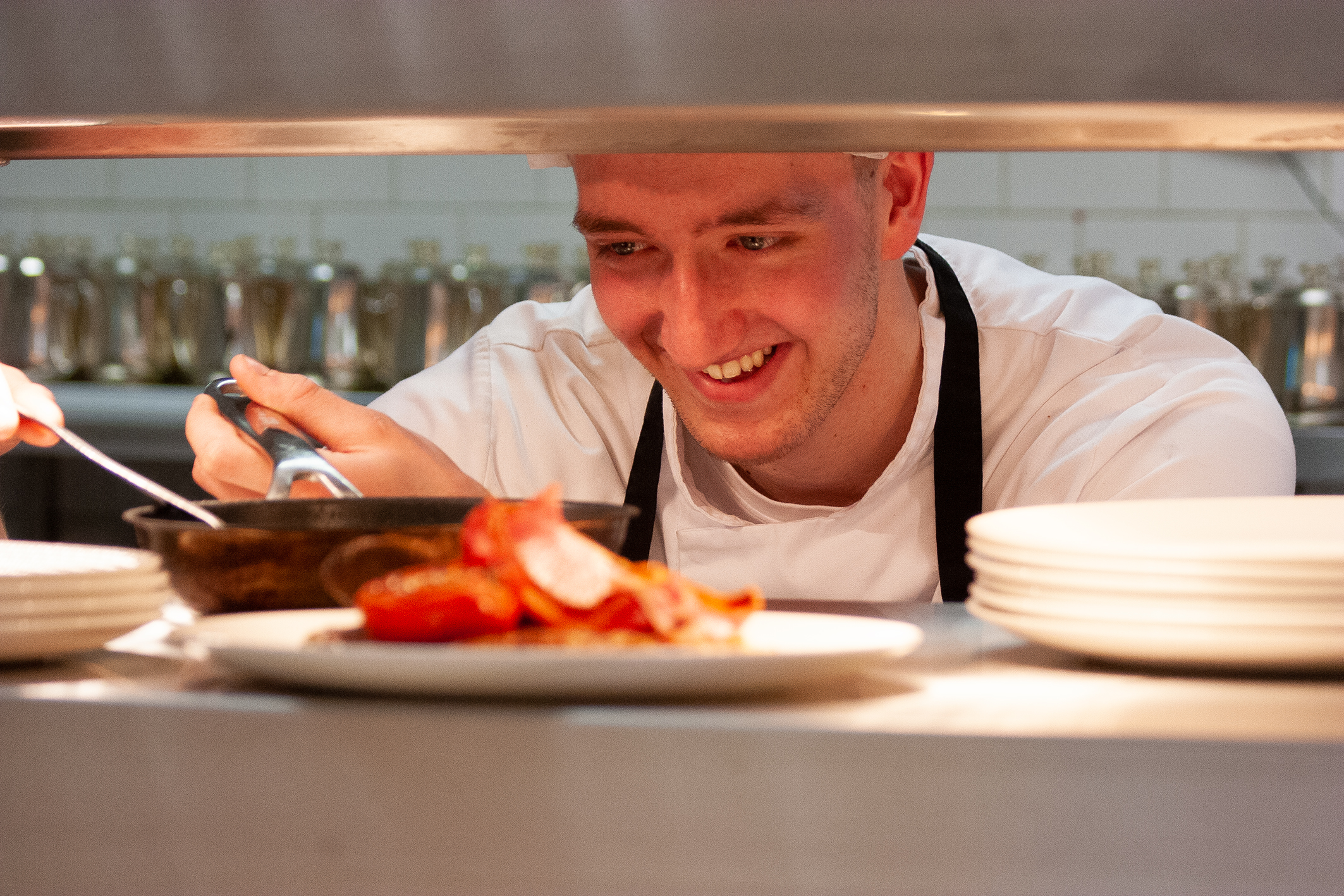A cook serving up a dish of food in a professional kitchen to be taken out to diners.