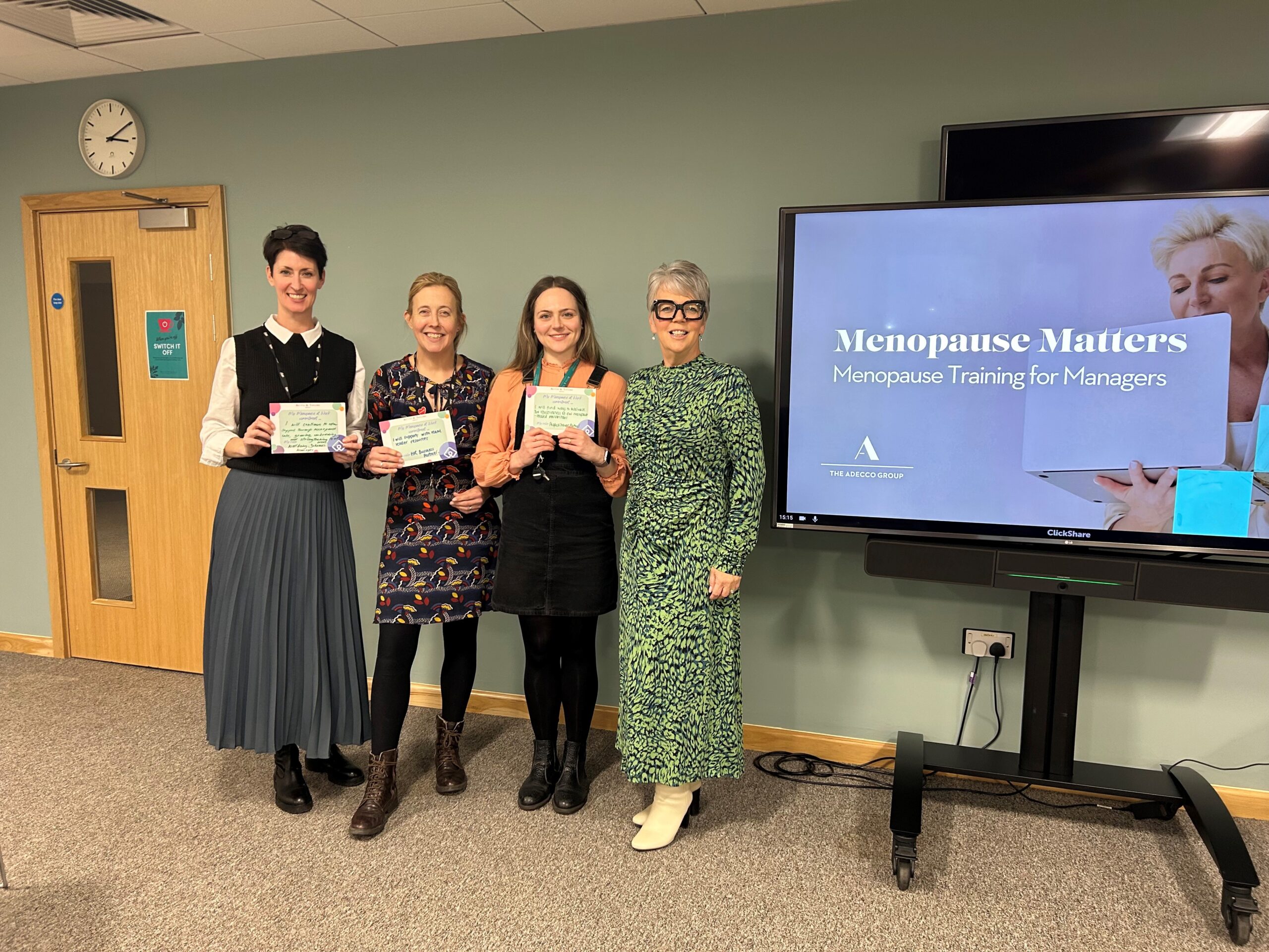 Three women standing in front of a TV screen showing a Powerpoint presentation.