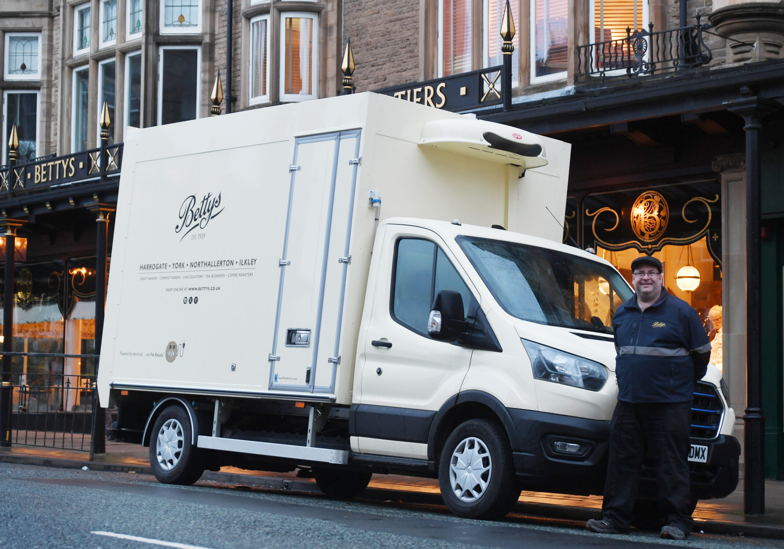 A Bettys delivery driver poses in front of a Bettys electric van