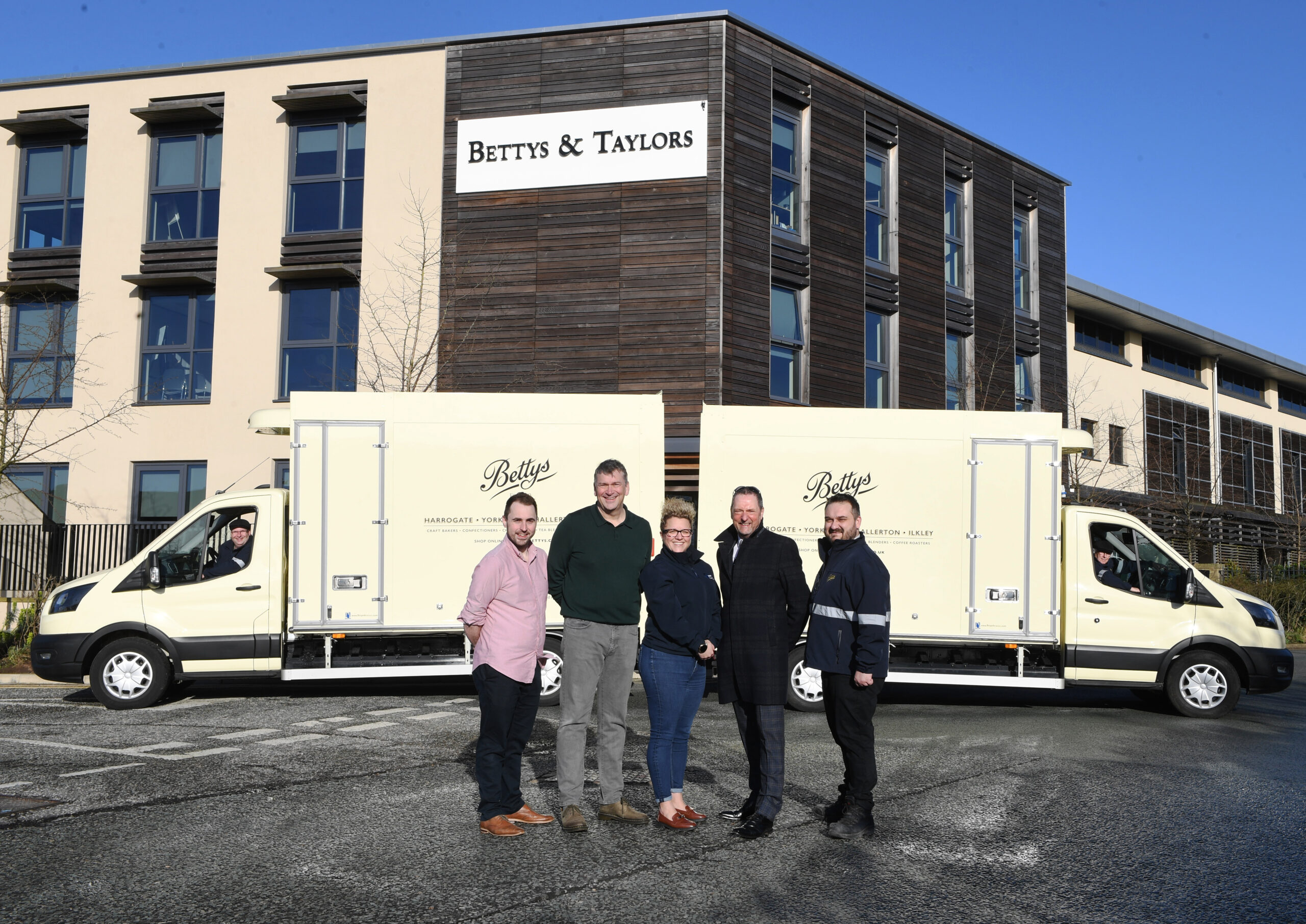 A team from Bettys and Prohire pose in front of two electric Bettys vans parked end to end.