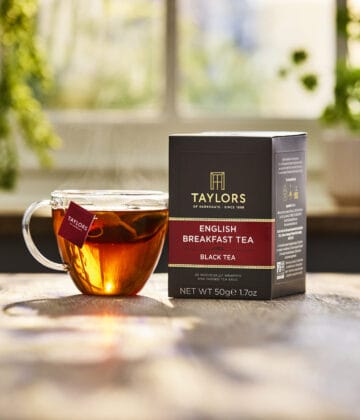 A glass tea cup holding a brewing tea with a box of Taylors of Harrogate tea next to it.